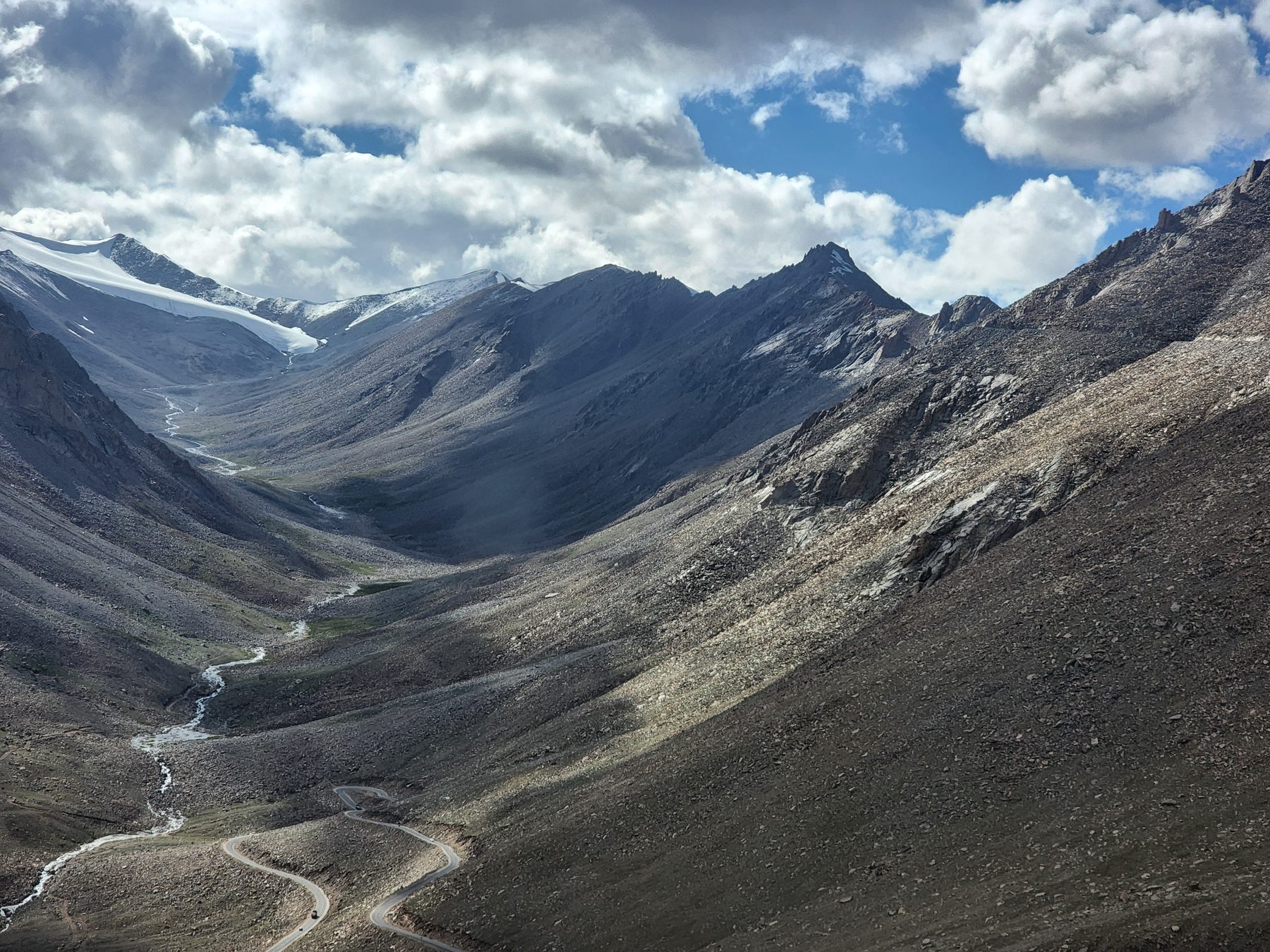 A vast glacial valley of grey scree with patches of snow and a winding road cutting through the bottom