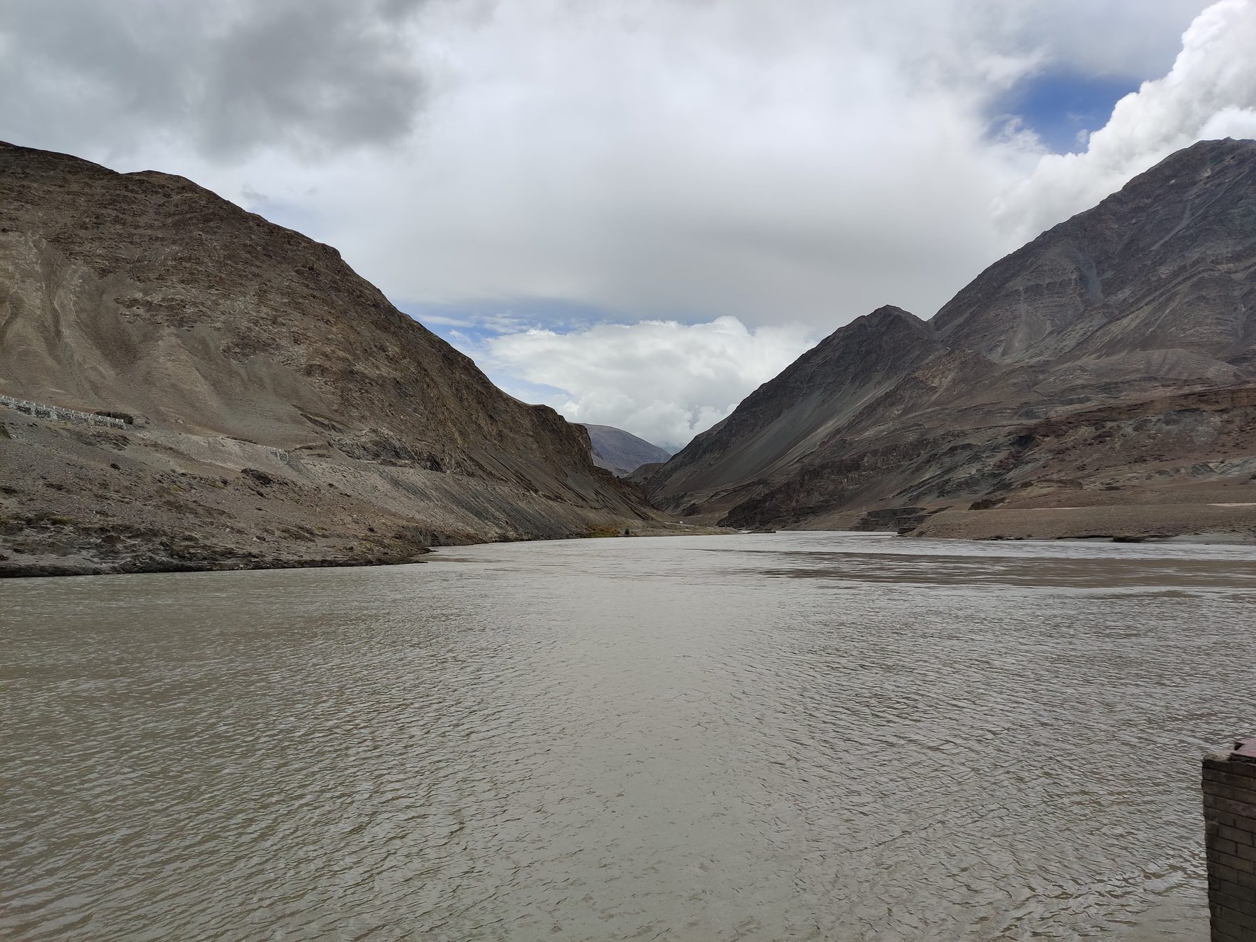 The Zanskar river wide and slow and brown between bare mountains under a grey sky